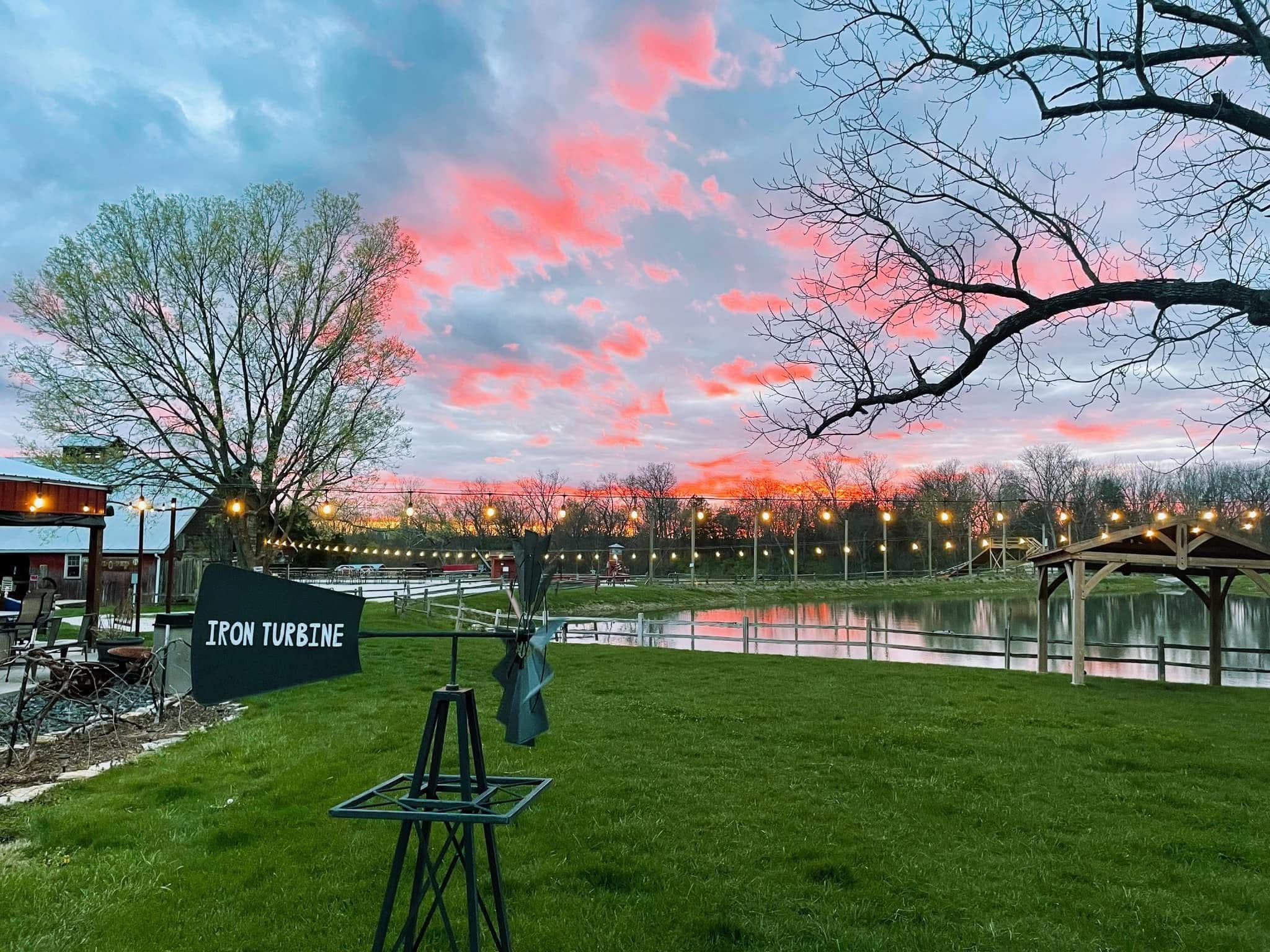 A pink sunset over the Iron Turbine lawn, pond, and string lights.